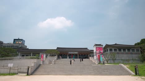 People-walk-down-the-stairs-of-the-National-Palace-Museum-Of-Korea-in-Gyeongbokgung-Palace-on-sunny-day---establishing-view
