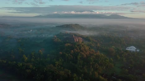 Majestic-drone-shot-of-famous-Borobudur-Temple-surrounded-by-dense-trees-and-mountain-range-in-background---Indonesia,Magelang