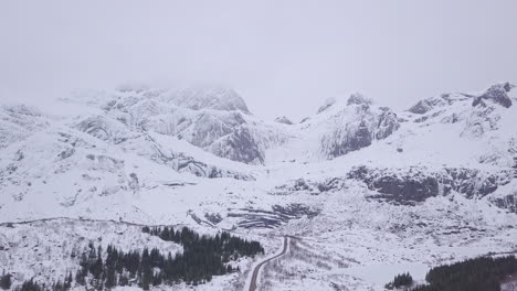 Aerial-backwards-shot-during-winter-of-the-scenic-road-to-Nusfjord,-Lofoten-Islands,-Norway