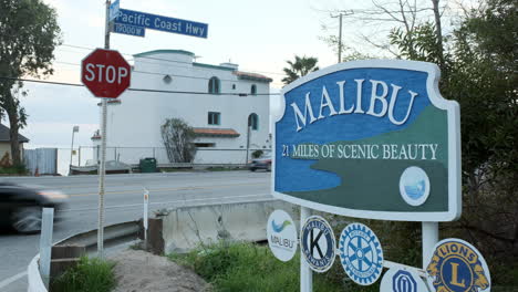 Tablero-De-Bienvenida-De-La-Ciudad-Escénica-De-Malibu-Kms,-Con-Tráfico-En-Movimiento-En-El-Fondo