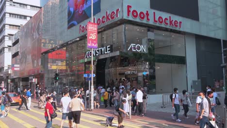 Chinesische-Fußgänger-Und-Käufer-Eilen-Und-Laufen-An-Einer-Hektischen-Und-Geschäftigen-Zebrastreifenkreuzung-Vor-Dem-Amerikanischen-Multinationalen-Sportbekleidungs--Und-Schuheinzelhändler-Foot-Locker-In-Hongkong