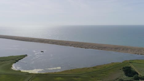 Aerial-rotating-and-tracking-from-right-to-left-above-the-fleet-lagoon-near-the-Abbotsbury-Swannery,-beside-Chesil-Beach,-Dorset