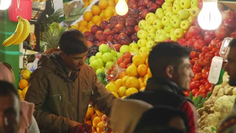 Joven-Comerciante-Organizando-Fruta-En-El-Puesto-Del-Mercado-Y-Saludando-A-Los-Clientes-En-El-Bazar-Tajrish-En-Teherán,-Irán