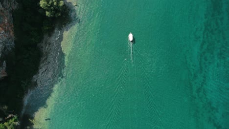Aerial-shot-of-a-boat-slowly-moving-on-turquoise-water-of-Ohrid-Lake-along-wild-Macedonian-coast-in-Southern-Europe