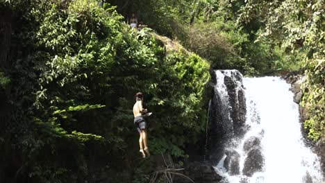 Toma-En-Cámara-Lenta-De-Un-Grupo-De-Turistas-Saltando-Del-Acantilado-En-La-Cascada-Alingaling-En-Bali,-Indonesia