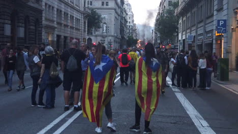 Two-girls-wearing-the-Estelada-flag-on-via-Laietana-during-the-Catalan-protest-with-a-big-fire-and-black-smoke-in-the-background