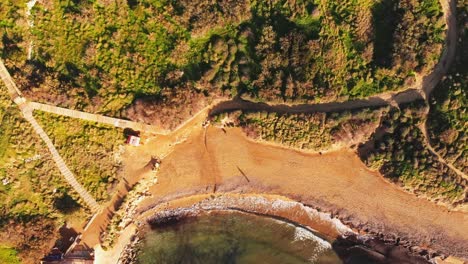 Aerial-drone-video-from-Malta,-showing-the-Ghajn-Tuffieha-beach-with-one-people-walking-with-long-shadows-before-sunset-at-winter