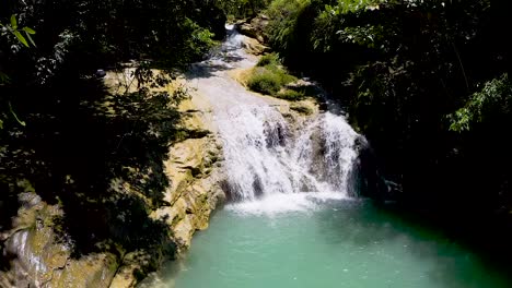 A-beautiful-waterfall-cascades-down-a-cliff-into-a-beautiful-turquoise-pool-below-in-the-middle-of-a-lush-green-jungle-in-Bohol,-Philippines