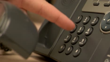 A-close-up-of-a-desk-office-phone-while-a-hand-pushes-buttons,-removes-the-receiver-and-places-it-back-on-the-base