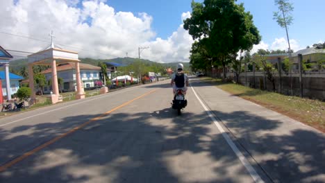 A-following-shot-of-a-man-riding-a-motorcycle-in-the-streets-of-the-island-of-Bohol,-Philippines