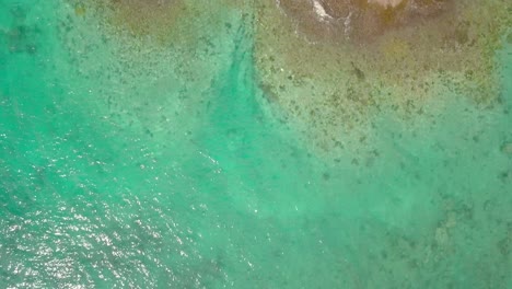 Aerial-top-down-view-over-trpoical-green-ocean,-and-rocky-island,-as-waves-wash-on-shore