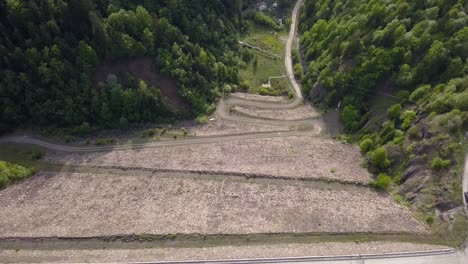 Aerial-Upwards-Panning-shot-of-swirving-road-cutting-through-woodland