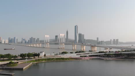 Drone-approach-shot-of-traffic-crossing-Sai-Van-Bridge-in-Macau-with-mainland-China-skyscrapers-in-background