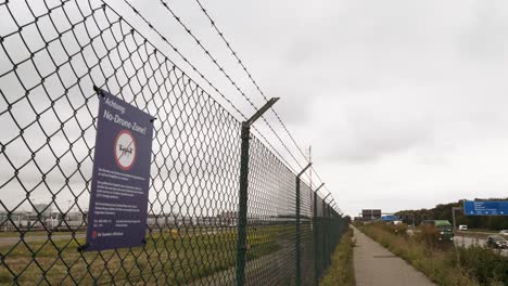 Drones-forbidden-sign-at-frankfurt,-germany-airport-fence-next-to-highway-a5-with-747-400-aircraft-airplane-passing