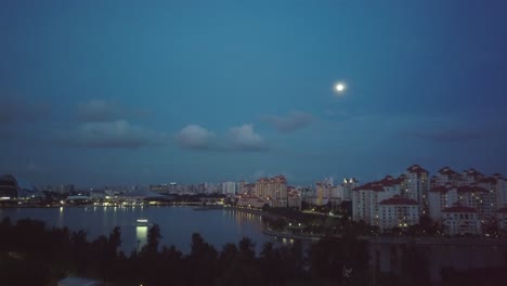 Toma-Aérea-De-Drones-En-Ascenso-De-Condominios-En-Singaproe-Por-La-Noche-Con-Luna-Llena