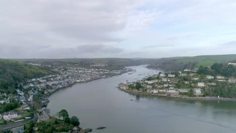 Forward-tracking-aerial-over-winter-thicketed-trees-towards-the-inlet-naval-tradition-town-of-Dartmouth,-Devon