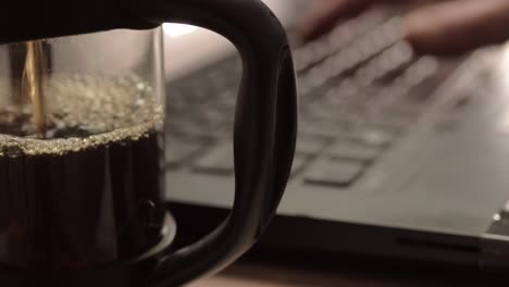 Pouring-fresh-coffee-into-a-pot-with-hands-typing-in-background