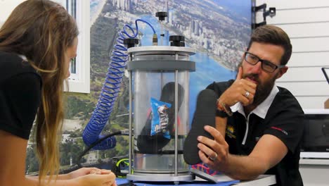 A-technician-demonstrating-a-pressure-test-on-a-item-while-a-female-observer-looks-on