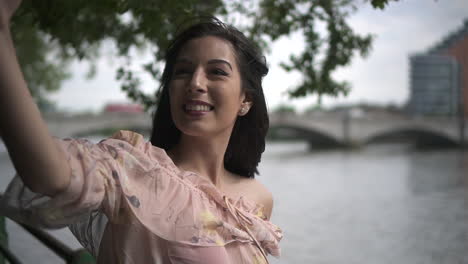 Close-Up-of-an-attractive-Hispanic-tourist-taking-a-selfie-of-the-Thames-in-London-from-a-river-side-walk,-holding-her-phone-to-frame-the-shot