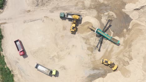 Top-aerial-view-of-bulldozer-loading-sand-into-empty-dump-truck-in-open-air-quarry