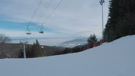 POV-perspective-of-snowboarder-travelling-downhill-on-white-resort-ski-slopes-under-ski-lifts