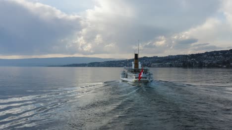 Drone-shot-orbiting-behind-Belle-Epoque-steam-boat-on-Lake-Léman,-Switzerland-at-sunset-Mirror-like-water-and-storm-clouds-in-the-background