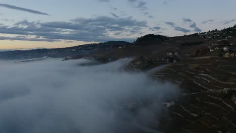 Aerial-over-fog-climbing-along-the-shore-of-Lake-Léman-and-Lavaux-Villette,-Lavaux---Switzerland
