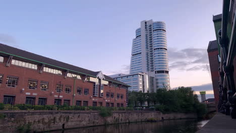 Zeitraffer-Des-Sonnenuntergangs-Hinter-Einem-Wolkenkratzer-In-Der-Stadt-Mit-Einem-Fluss-Im-Vordergrund