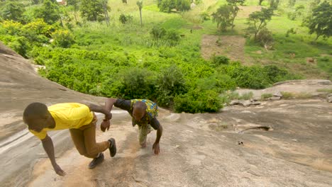 Two-African-men-help-each-other-up-a-very-steep-granite-rock-climb-in-East-Africa