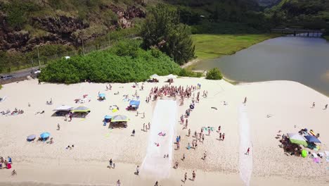 Drone-Shot-moving-towards-a-crowd-on-people-on-the-beach-surrounding-a-slip-n-slide-that-leads-down-to-the-water