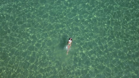 Woman-in-a-bikini-swims-and-splashes-in-the-green,-shimmering-waters-of-the-Aegean-Sea