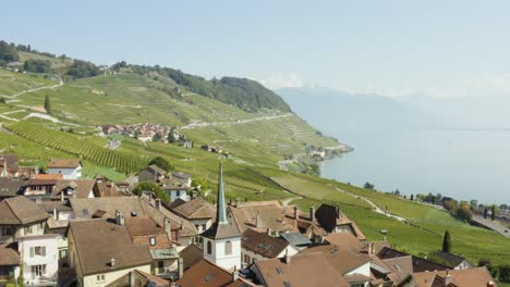 Overflying-typical-swiss-village-in-Lavaux-vineyard,-passing-close-to-church-bell-tower---Switzerland