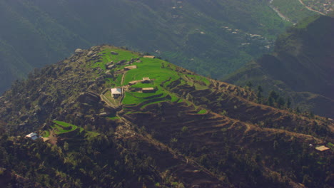 Houses-at-top-of-the-mountain,-beautiful-drone-view,-green-hills-with-living-people