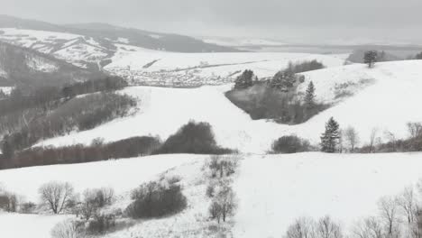 Aerial-forward-through-snowed-in-hill-landscape-with-town-and-river-in-distance