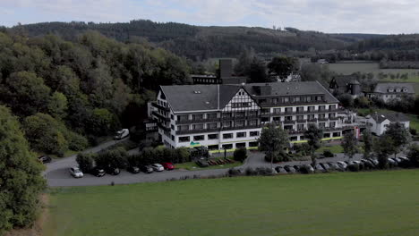 Aerial-view-of-the-Alpin-hotel-in-the-spa-and-ski-village-of-Grafschaft-in-the-Sauerland-region-near-Winterberg-against-a-blue-sky-with-clouds