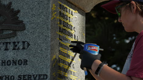 Female-restoration-artist-repairs-the-painted-lettering-on-a-world-war-memorial