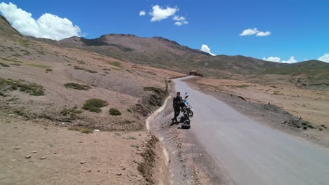 Man-parked-with-motorcycle-on-empty-asphalt-road-leading-to-komic-village-in-the-Himalayan-mountains-of-Spiti-Valley-India,-aerial