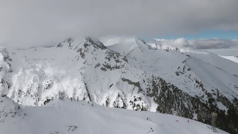 Schwenkende-Zeitlupen-Panorama-Drohnenaufnahme-Mit-Skifahrern-Und-Snowboardern-Entlang-Des-Bergrückens