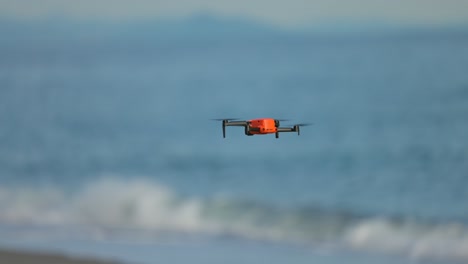 Orangefarbene-Kleine-Drohne,-Die-über-Das-Ufer-Eines-Strandes-Fliegt