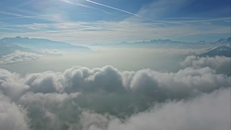Fluffy-skyscape-above-mountain-range-with-shining-sun,-aerial-view