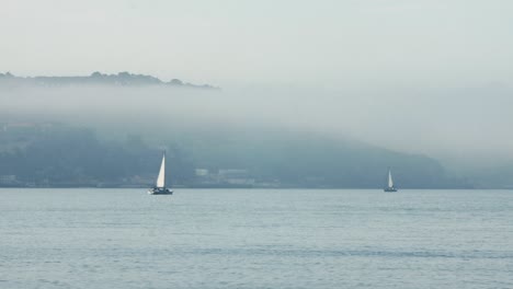 Sailing-Boats-Middle-Of-Blue-River-In-Foggy-Scene,-Lisbon-City,-Portugal