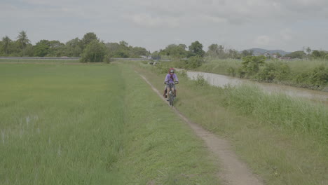 Lone-female-bikes-on-dirt-path-in-grassy-field-of-Alor-Setar-Malaysia