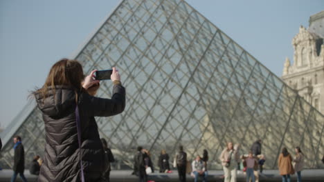 Foreign-tourist-takes-a-photo-with-smartphone-of-the-louvre-pyramid-in-Paris