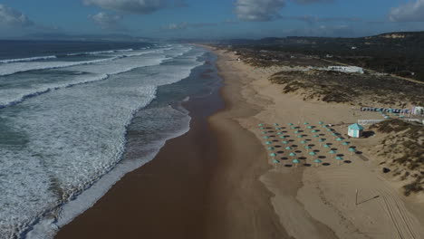 Drone-shot-of-Costa-da-Caparica-near-Lisbon---drone-is-flying-along-the-coast,-passing-beach-clubs