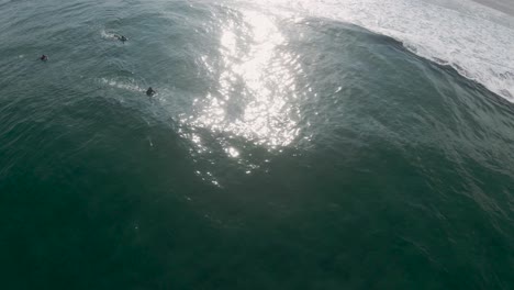Aerial-orbit-of-glistening-sunlight-on-ocean-water-as-bodyboarders-swim
