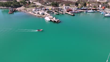 Aerial-pan-of-motorboat-entering-harbor-with-green-water-and-large-boats