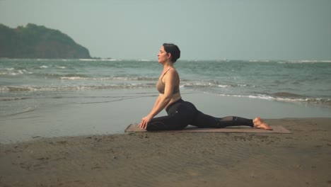 Pigeon-yoga-position-woman-on-a-beach-exercising-asana,-Eka-Pada-Rajakapotasana-outdoors