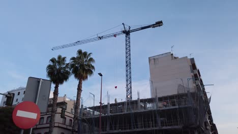 Tilt-Up-of-crane-high-above-building-under-construction-in-Seville,-Spain