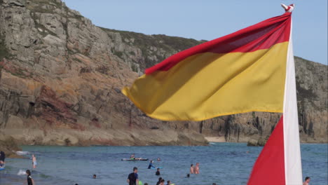Eine-Rot-gelbe-Rettungsschwimmerfahne-Weht-Und-Tanzt-Im-Wind-Am-Strand-Von-Perranuthuoe-In-England-–-Weitwinkelaufnahme