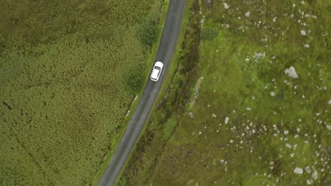 Cinematic-aerial-tracking-shot-of-single-white-car-traveling-through-green-countryside